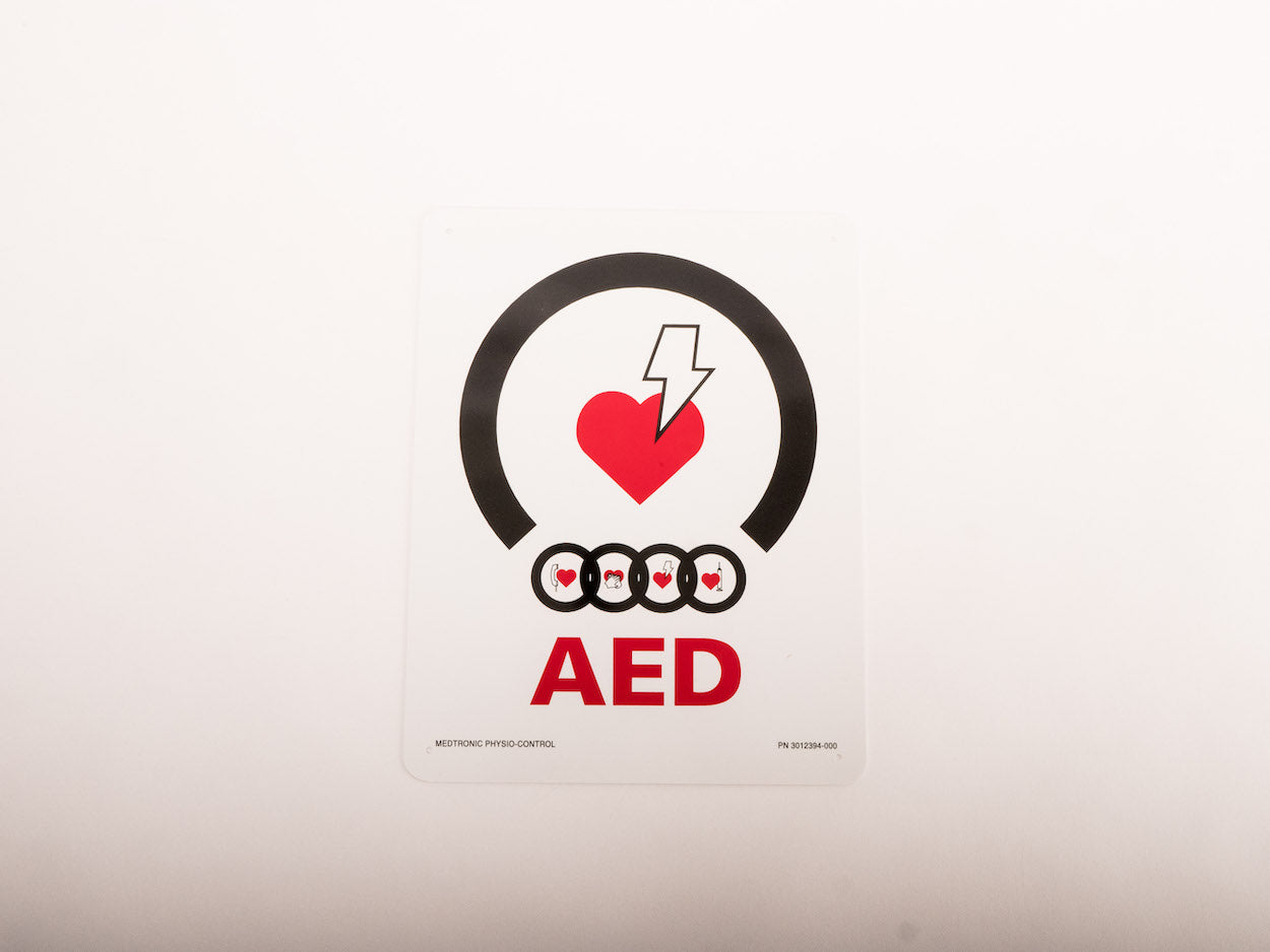 A white universal AED wall mount bracket with black straps and red signage