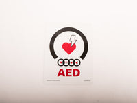 A white universal AED wall mount bracket with black straps and red signage