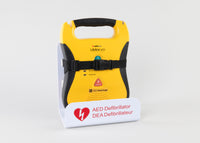 A black and yellow Defibtech Lifeline AED strapped into a white metal wall mount bracket