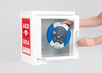 A blue and white HeartSine AED being retrieved by hand from a white metal cabinet with red decals